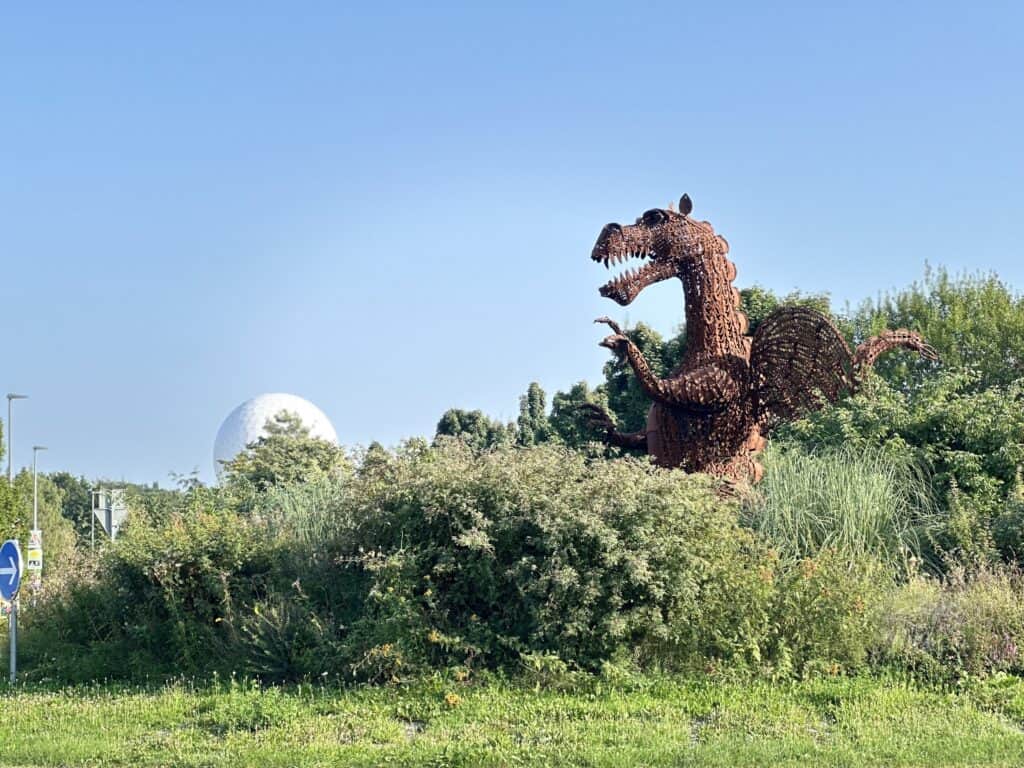 Metall-Drachen-Skulptur in Wachtberg, umgeben von Natur und Büschen.