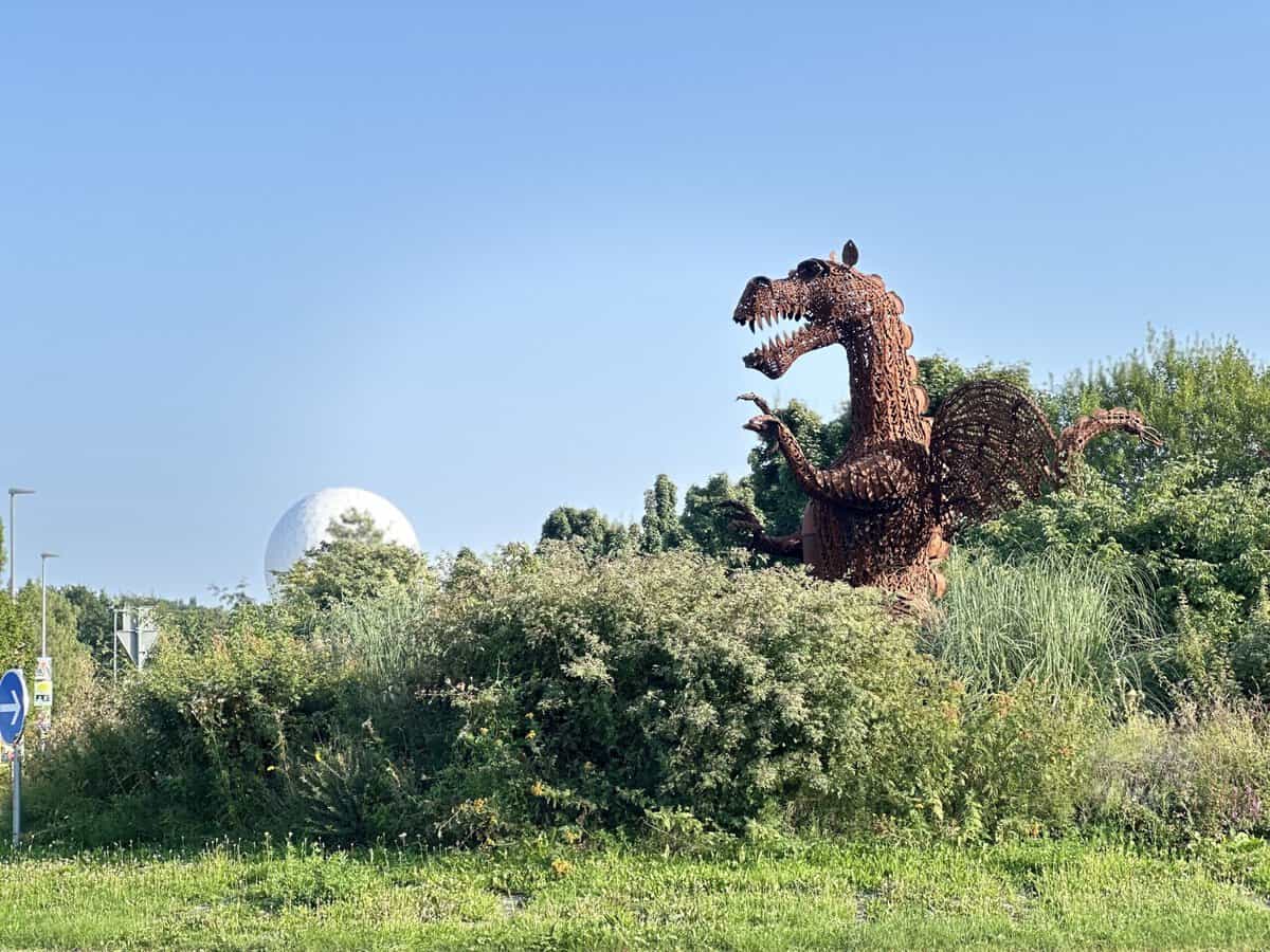 Metall-Drachen-Skulptur in Wachtberg, umgeben von Natur und Büschen.
